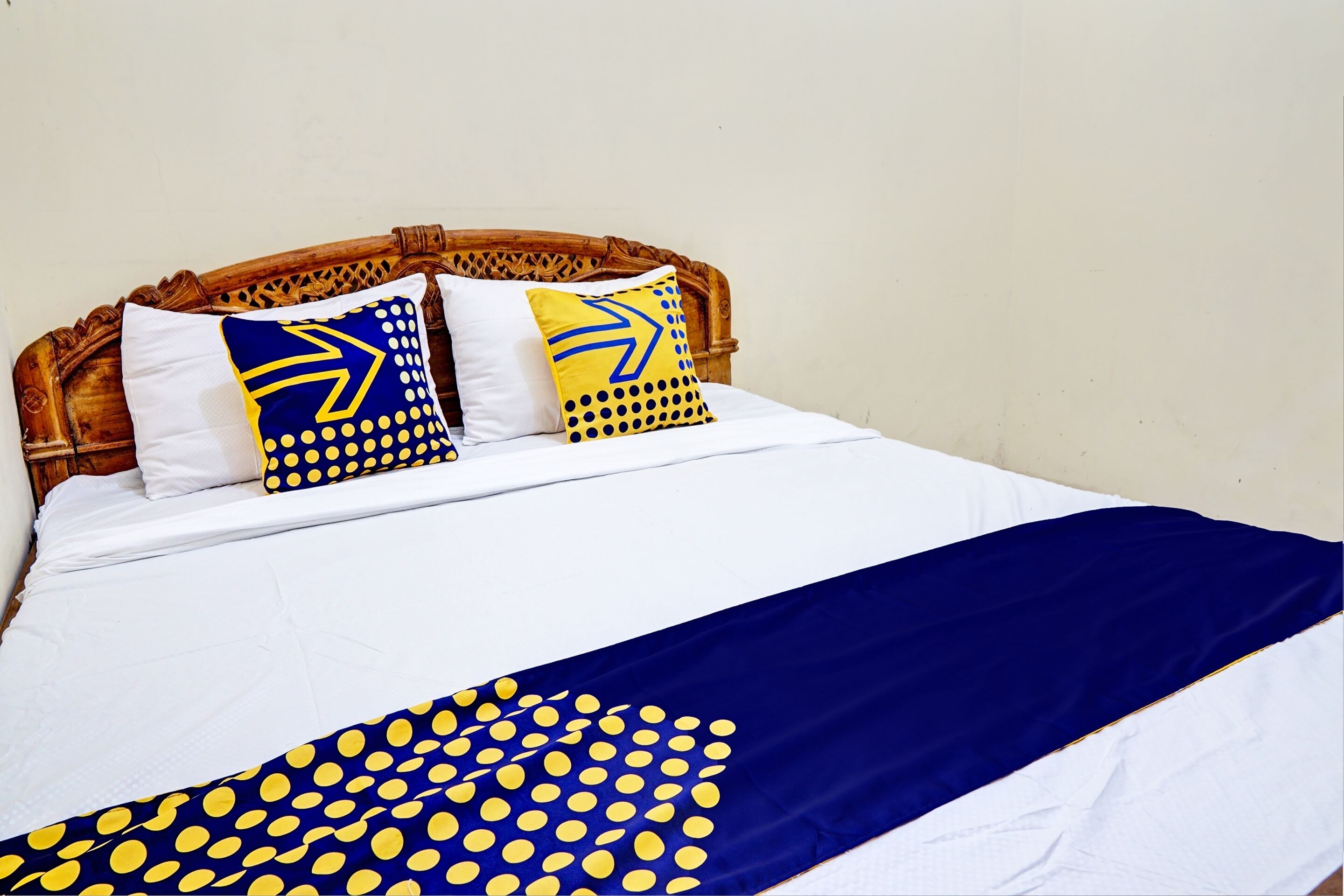 A bed with a white mattress, a blue and yellow polka dot blanket, and two pillows with blue and yellow patterns.
