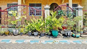 A building with a tiled facade, a gated entrance, and various potted plants in front. - OYO 93108 Homestay H Syarif Syariah – RA Kartini (Gresik)