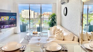 Un salón moderno con un sofá, una mesa de comedor preparada para cuatro personas y un televisor mostrando un programa.
