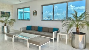 Una sala de estar moderna con un sofá, dos mesas de centro y ventanas amplias que dan a una vista de la ciudad.