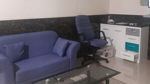Une pièce avec un canapé bleu, une table basse noire en métal ajouré, un bureau blanc avec des tiroirs et un climatiseur fixé au mur.