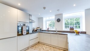 A modern kitchen with white cabinets, a herringbone floor pattern, a stainless steel range hood, and a large window providing natural light. - Stunning Executive 2 Bedroom House (Worksop)