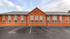 A brick building with a symmetrical facade, large windows, and a parking lot with marked spaces. - Stunning Executive 2 Bedroom House (Worksop)