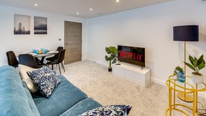 A modern living room with a sofa, a dining table, and a TV displaying 'NETFLIX'. - Stunning Executive 2 Bedroom House (Worksop)