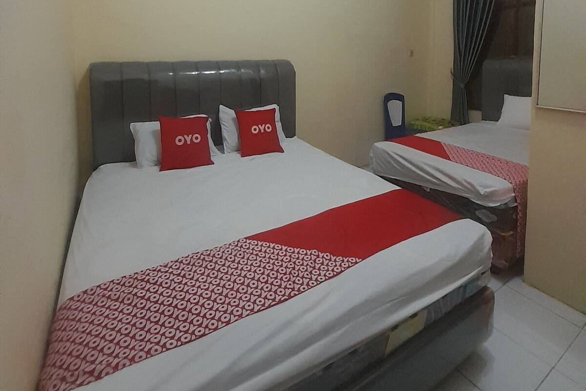 A hotel room with two beds, each with a red and white patterned bedspread, and a grey headboard.