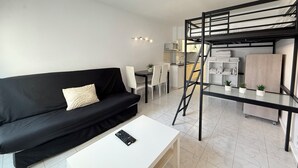 A compact living space with a black sofa, a white coffee table, a bunk bed, a kitchenette, and a dining area. - Agi Estrella de Mar 2 Apartamento for rent in Roses Girona. (Roses)