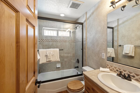 A bathroom with a glass-enclosed shower, a wooden toilet, and a sink with a mirror.