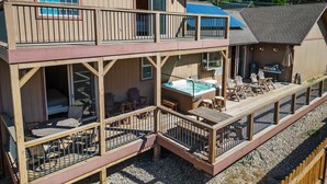 A two-story wooden cabin with a deck, outdoor seating, and a hot tub. - Hot Tub, Game Room, Large Deck w/ Mountain Views, 4BDR | Paw Print by AvantStay (Big Bear Lake)