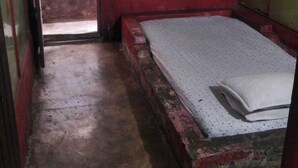A small, dimly lit room with a single bed, a window with a red frame, and a concrete floor. - Hotel O Barak Tambunan NearBelawan Port (Medan)