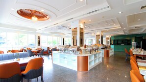 Een ruime hotel eetzaal met diverse zithoeken, een centraal buffet en uitzicht op het buitenland door grote ramen.