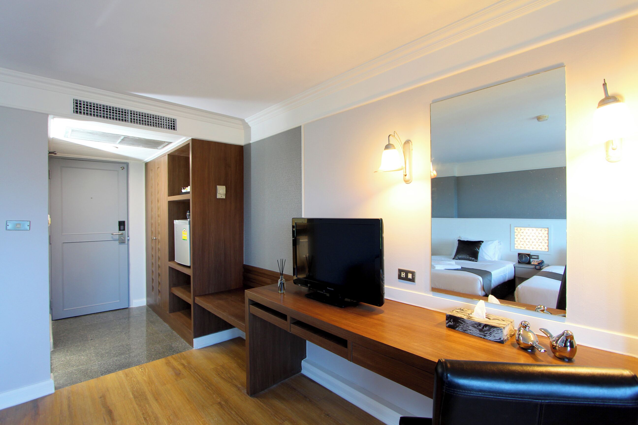 A hotel room with a wooden desk, a television, a mirror, and a bed with a nightstand.