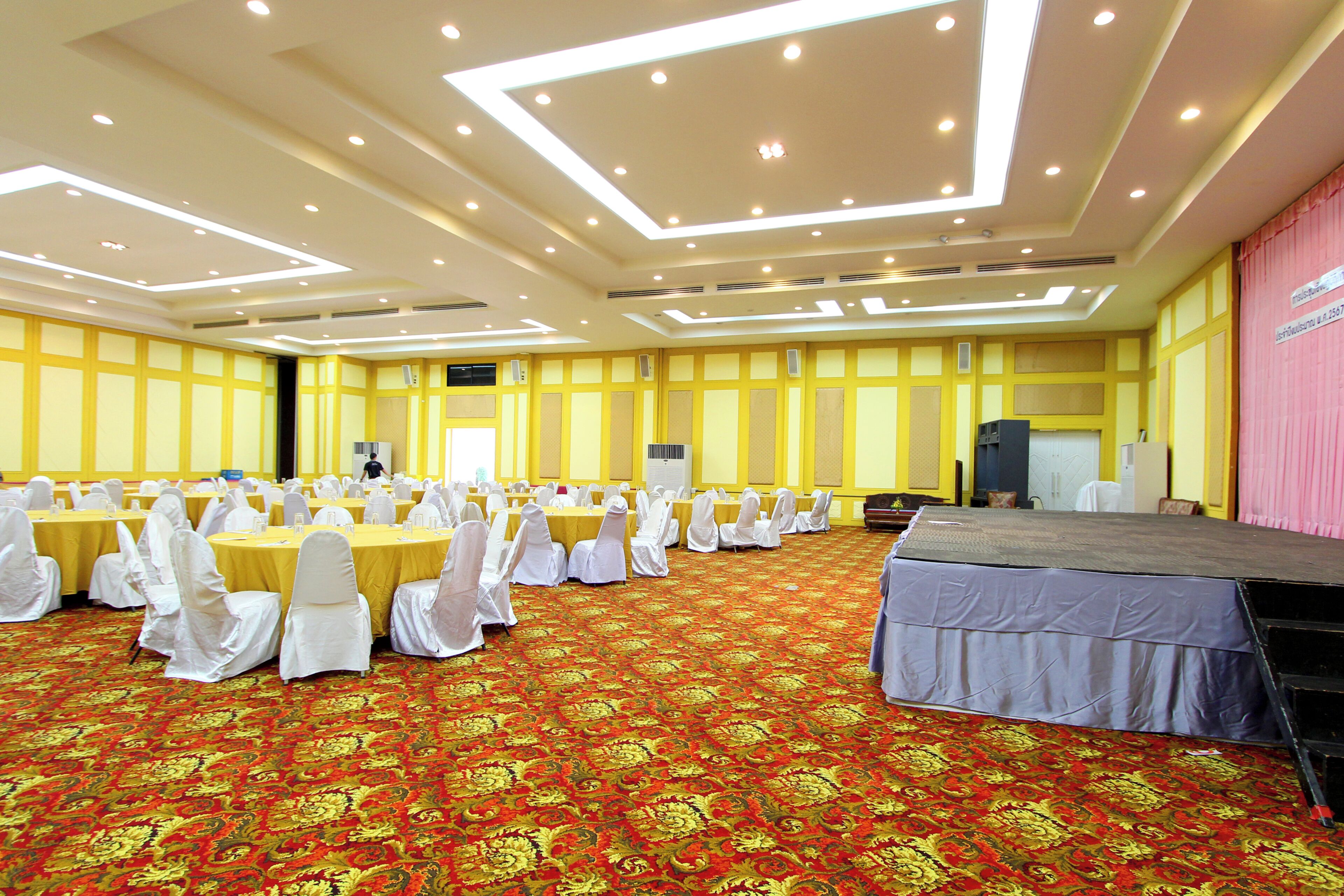 A conference room with tables and chairs, a stage, and a patterned carpet.