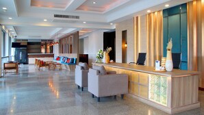 Een moderne hotelentree met een receptiebalie, een zithoek en een groot raam.