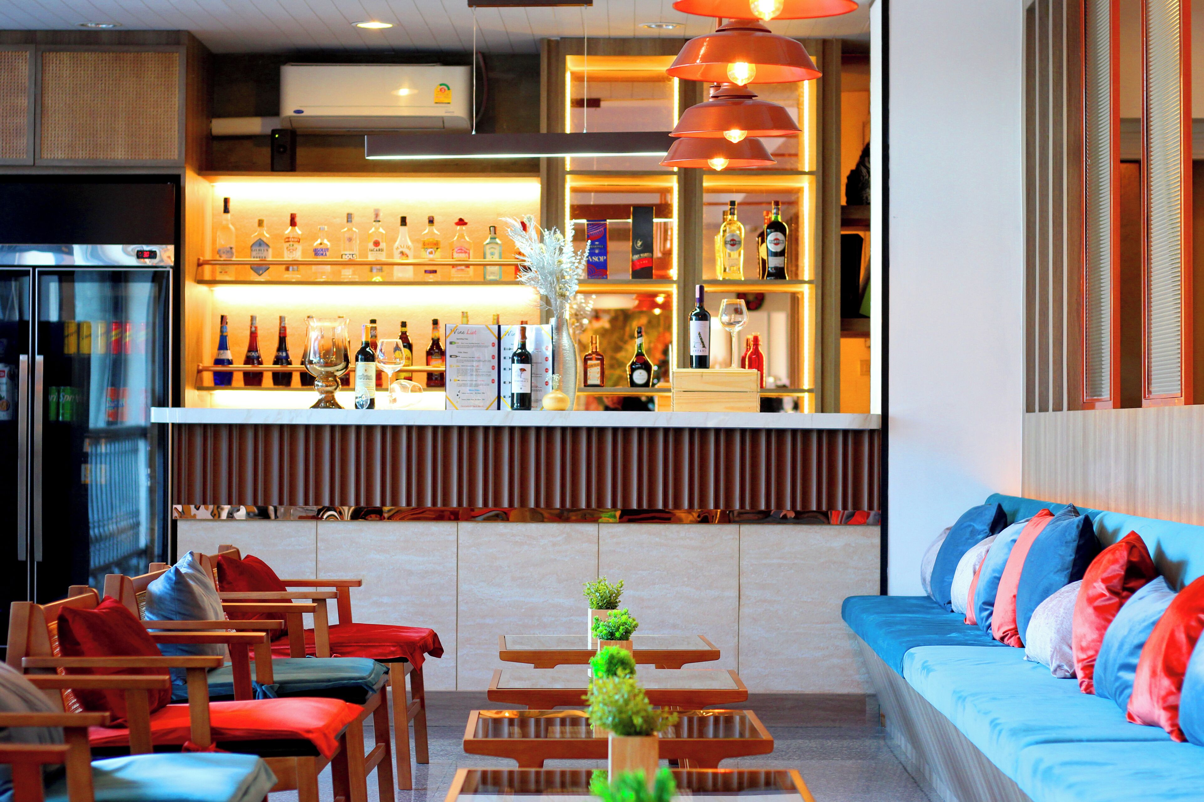 Zona de bar con estantes de botellas de licor, un refrigerador y asientos con cojines.