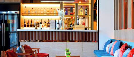 Zona de bar con estantes de botellas de licor, un refrigerador y asientos con cojines.