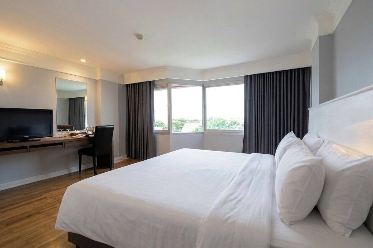 Una habitación de hotel con una cama grande, un escritorio con televisor y una ventana con cortinas.