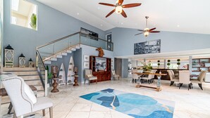 A spacious living area with a high ceiling, a staircase, and a dining area with modern furniture. - Sea Horizon (San Pedro)