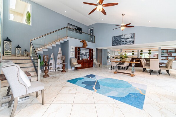 A spacious living area with a high ceiling, a staircase, and a dining area with modern furniture. - Sea Horizon (San Pedro)
