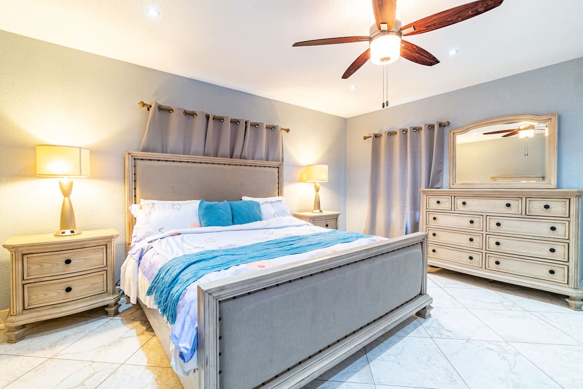 A bedroom with a bed, nightstands, a dresser, a ceiling fan, and a mirror.