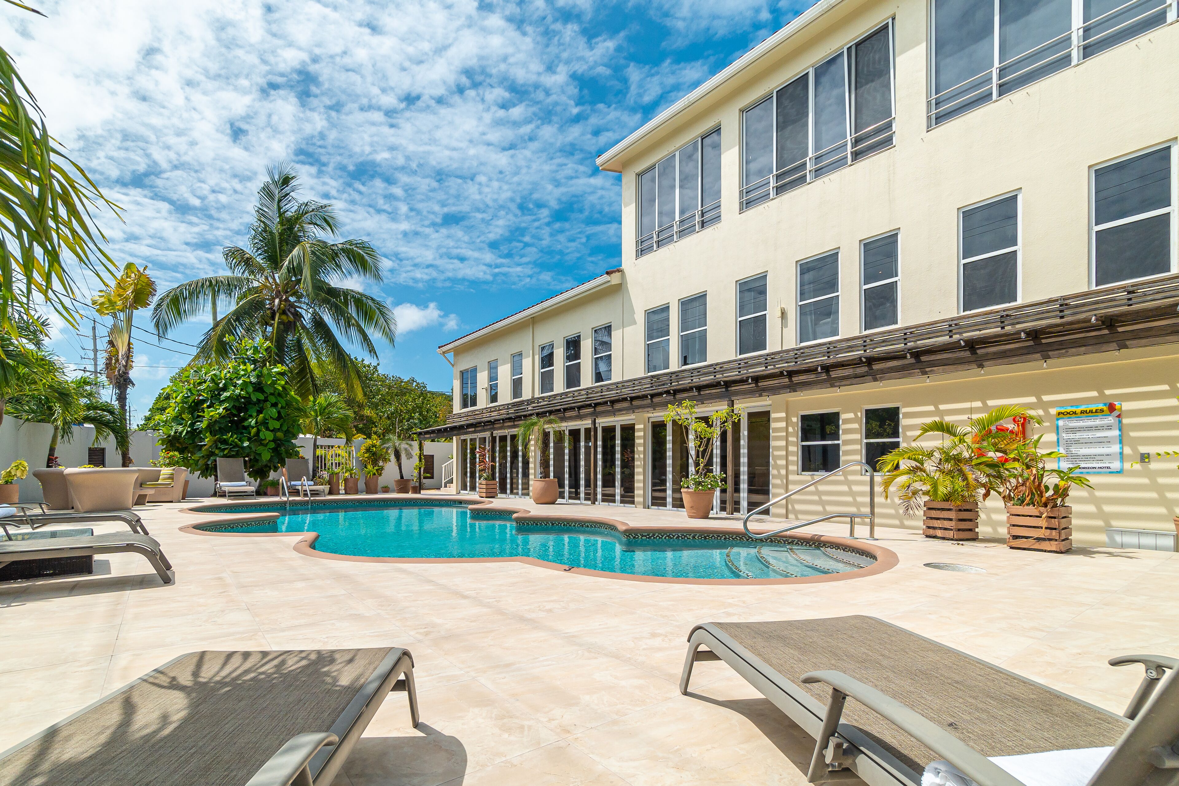 A pool area with lounge chairs, a swimming pool, and a building with multiple windows and a balcony.