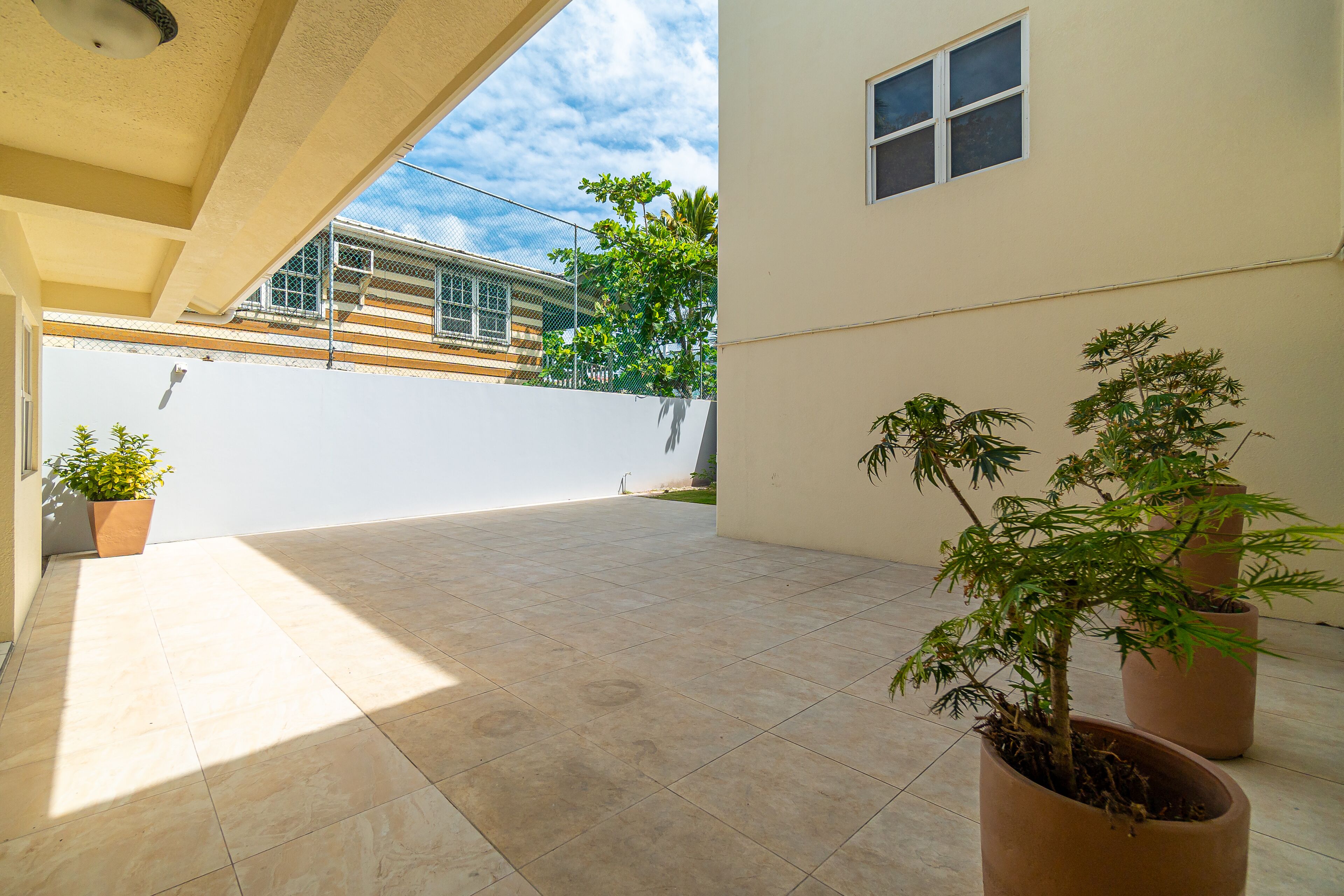 Eine großzügige Terrasse mit Fliesenboden, Topfpflanzen und Blick auf ein Gebäude mit weißer Fassade und einem Fenster.