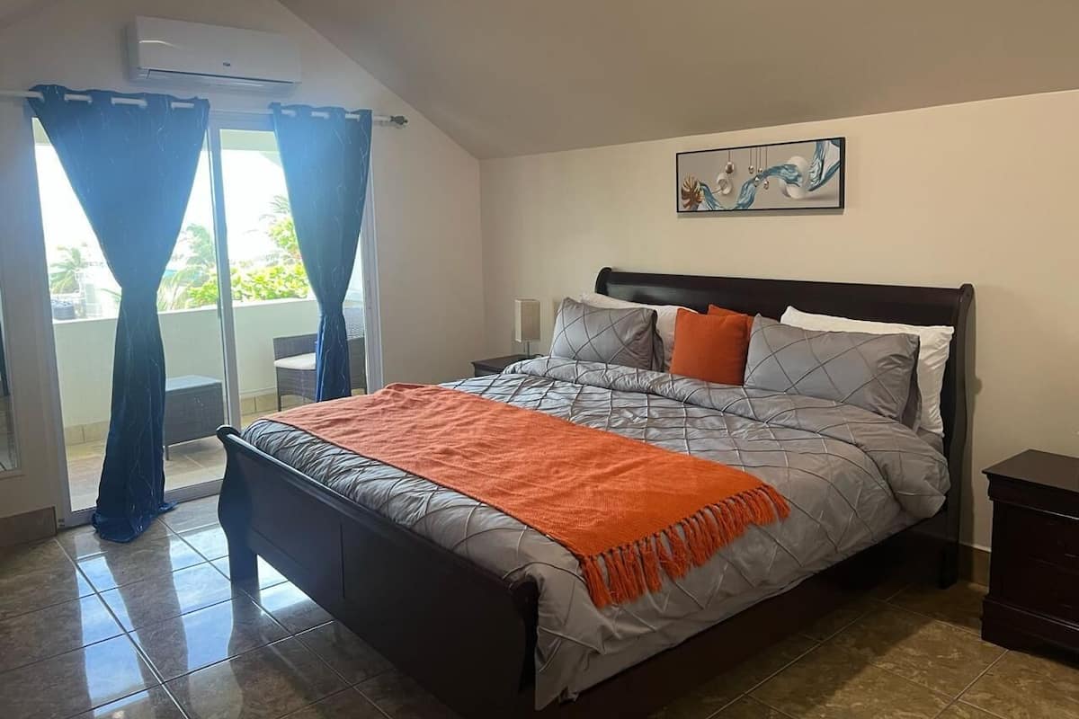 A bedroom with a bed, curtains, a painting, and a nightstand.