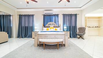 A bedroom with a large bed, two ceiling fans, a bench, a chair, and a walk-in closet.