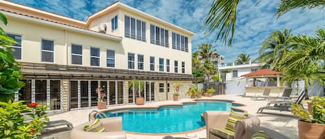 A pool area with lounge chairs, a swimming pool, and a building with multiple windows and a balcony.