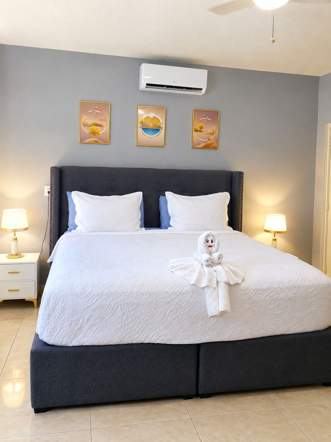 Ein Hotelzimmer mit einem Bett, zwei Nachttischlampen, einer Klimaanlage und drei gerahmten Bildern an der Wand.