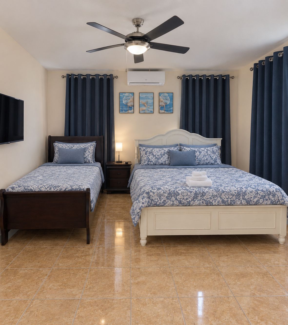 A bedroom with two single beds, a ceiling fan, a flat-screen TV, and a wall-mounted air conditioner.