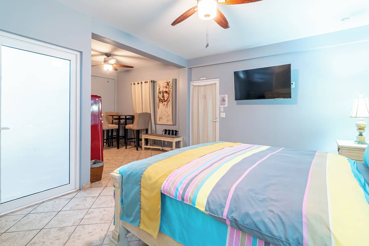 A bedroom with a bed, a ceiling fan, a TV, and a desk with chairs.