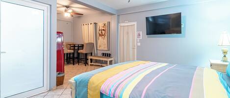 A bedroom with a bed, a ceiling fan, a TV, and a desk with chairs.
