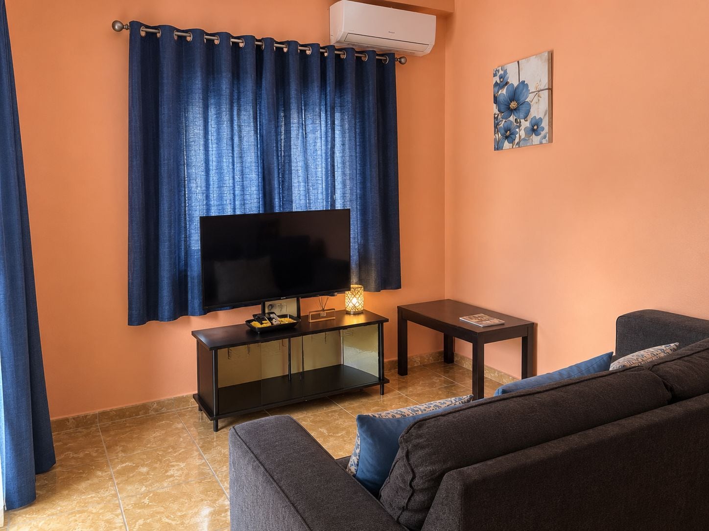 Ein Wohnzimmer mit Flachbildfernseher, einem kleinen Beistelltisch, einer Couch und einer dekorativen Lampe.
