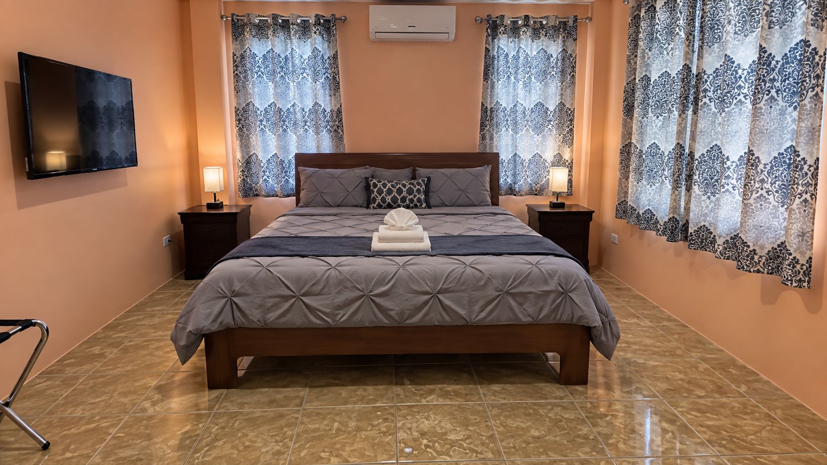 Une chambre à coucher avec un lit, deux tables de chevet, un téléviseur et des rideaux à motifs.