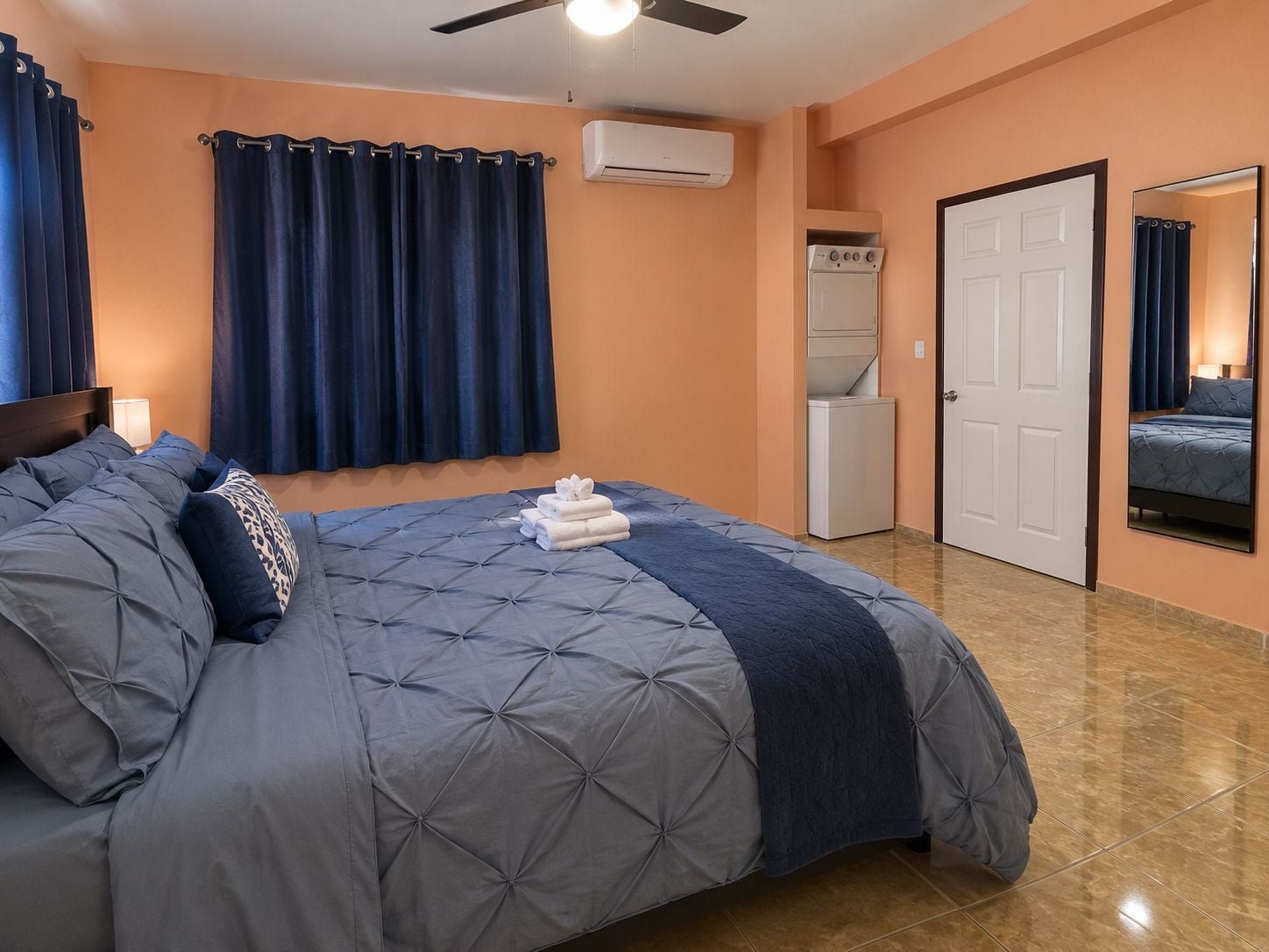 A bedroom with a bed, a ceiling fan, an air conditioning unit, a washing machine, and a door.
