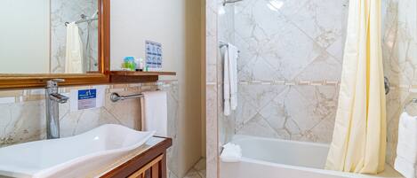 A bathroom with a large mirror, a sink, a bathtub, and a shower area.