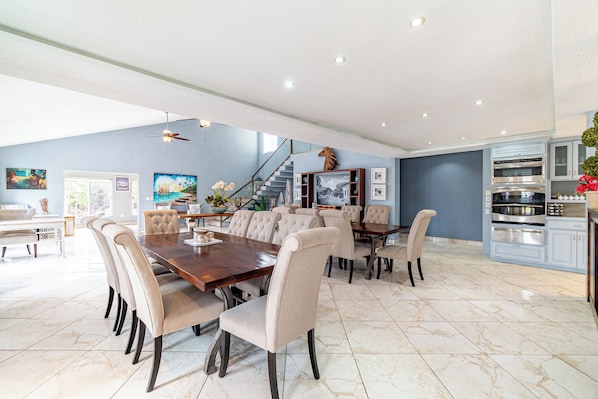A spacious dining area with a large wooden table and beige upholstered chairs, a kitchen with modern appliances, and a staircase leading to an upper level. - Sea Horizon (San Pedro)