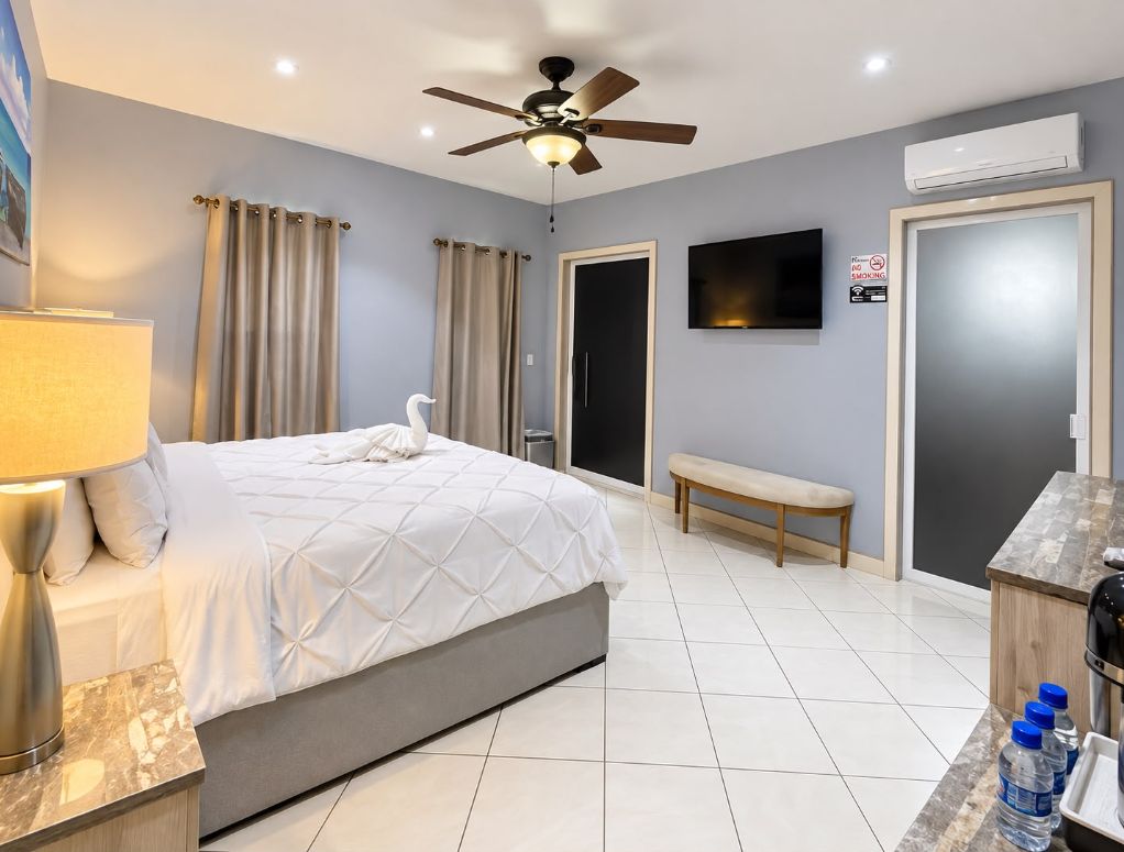 Habitación de hotel con una cama, un banco, un televisor y un escritorio con botellas de agua.