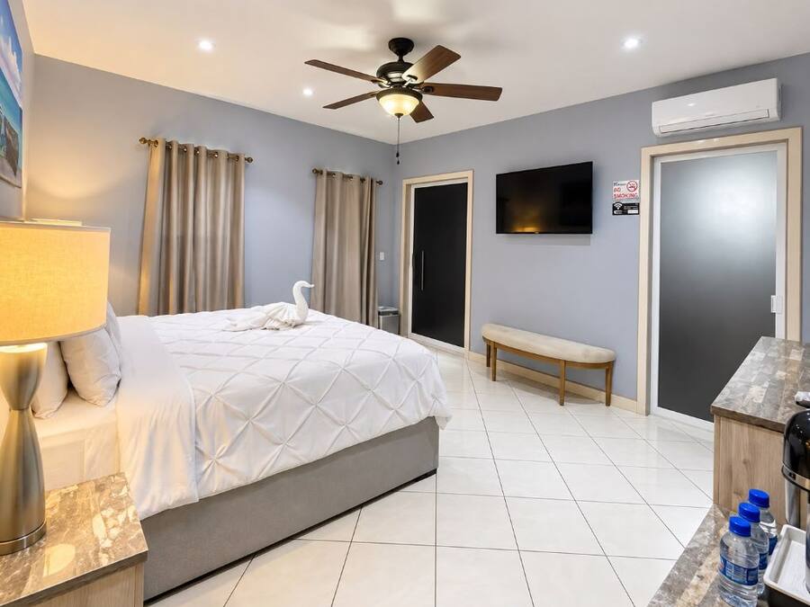 Habitación de hotel con una cama, un banco, un televisor y un escritorio con botellas de agua.