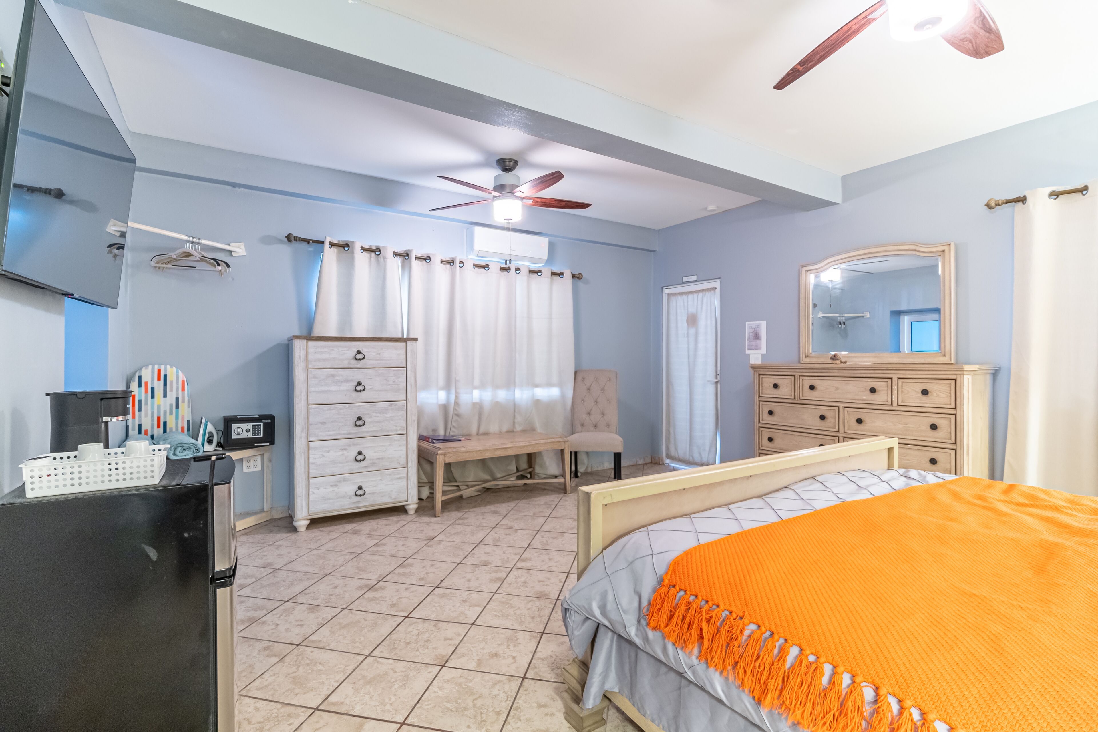 A bedroom with a bed, a ceiling fan, a dresser, a chair, a desk, and a mirror.