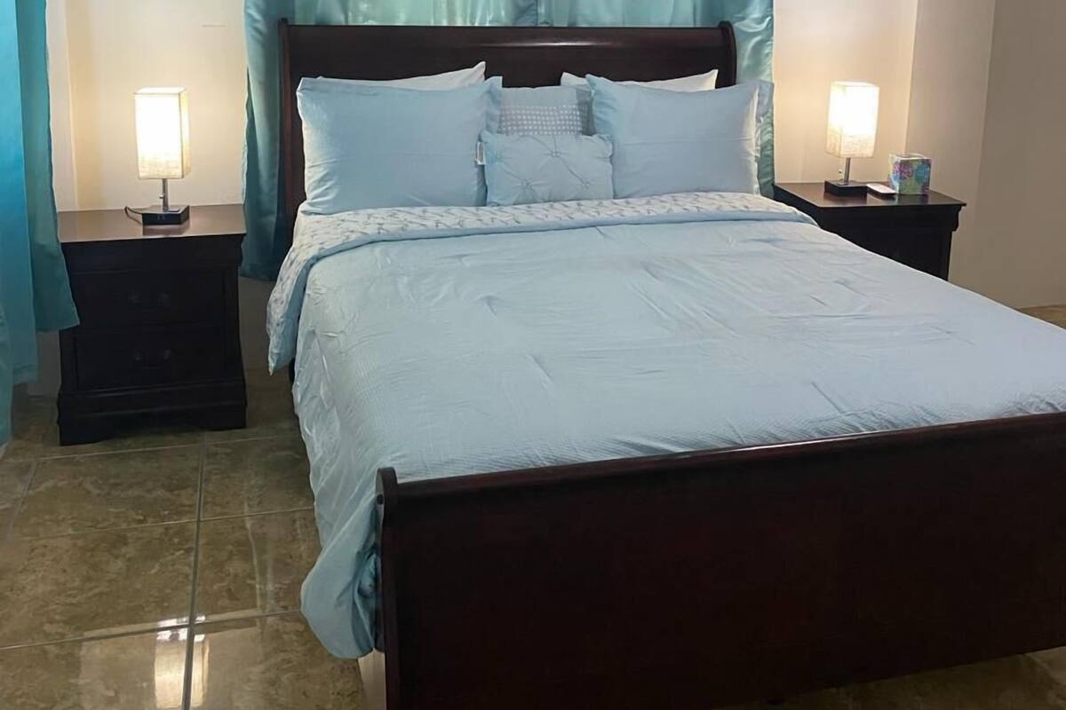 A neatly made bed with a wooden headboard, two bedside tables with lamps, and light blue curtains.