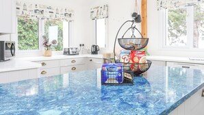 A modern kitchen with a blue marble countertop, white cabinetry, and a window with a view of greenery. - Pine Lodge (Colwyn Bay)