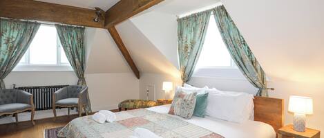 A cozy bedroom with a wooden ceiling, a large bed with floral bedding, two bedside tables with lamps, and a radiator.