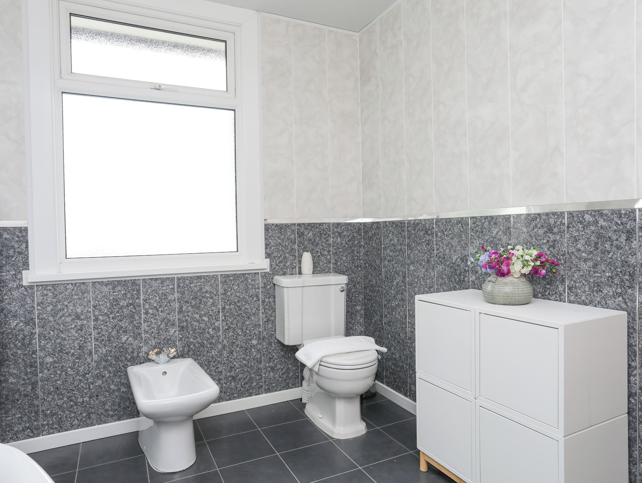 A modern bathroom with a toilet, bidet, and cabinet.