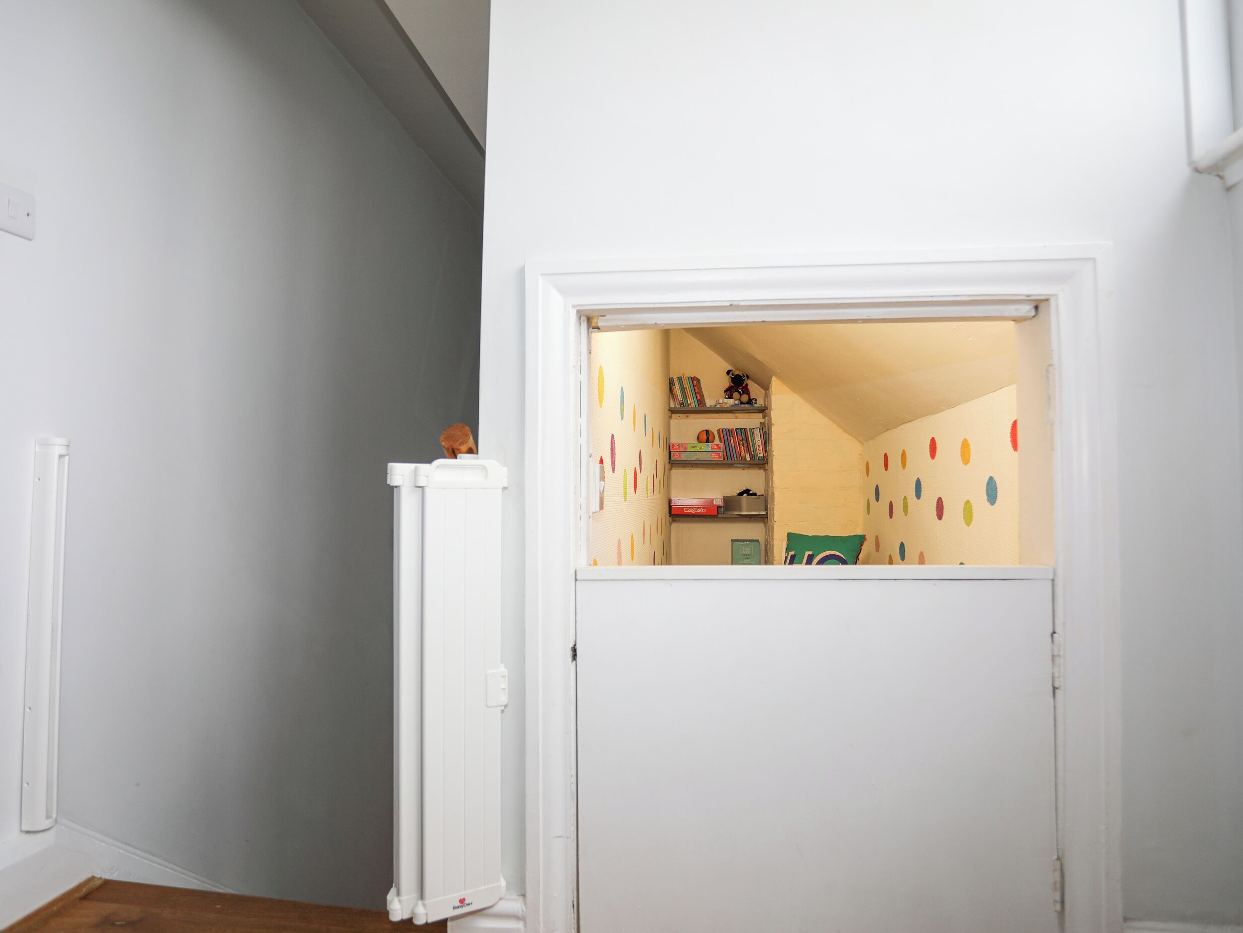 A small, enclosed room with a white door, a radiator, and shelves with books and toys.