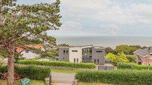 A modern two-story house with a view of the sea, surrounded by well-maintained hedges and a tree. - Pine Lodge (Colwyn Bay)