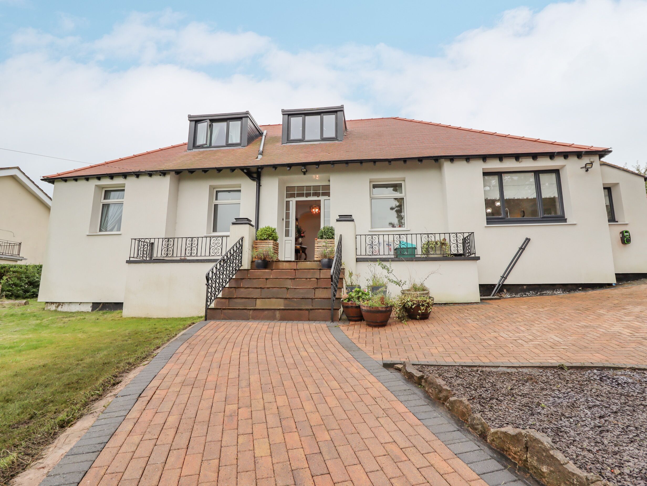 A two-story house with a brick pathway leading to the entrance, a small porch with potted plants, and a metal railing on the side.