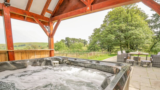 Un bain à remous doté d’une terrasse en bois et d’un espace salon extérieur, le tout entouré de verdure.