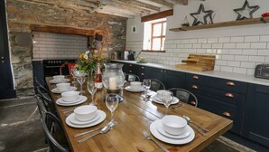 Un coin repas avec une table en bois dressée pour six personnes, entouré d’armoires bleu foncé et d’un mur en pierre.