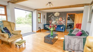 Un salon spacieux avec une grande fenêtre, un canapé bleu, un fauteuil vert et un plancher en bois.
